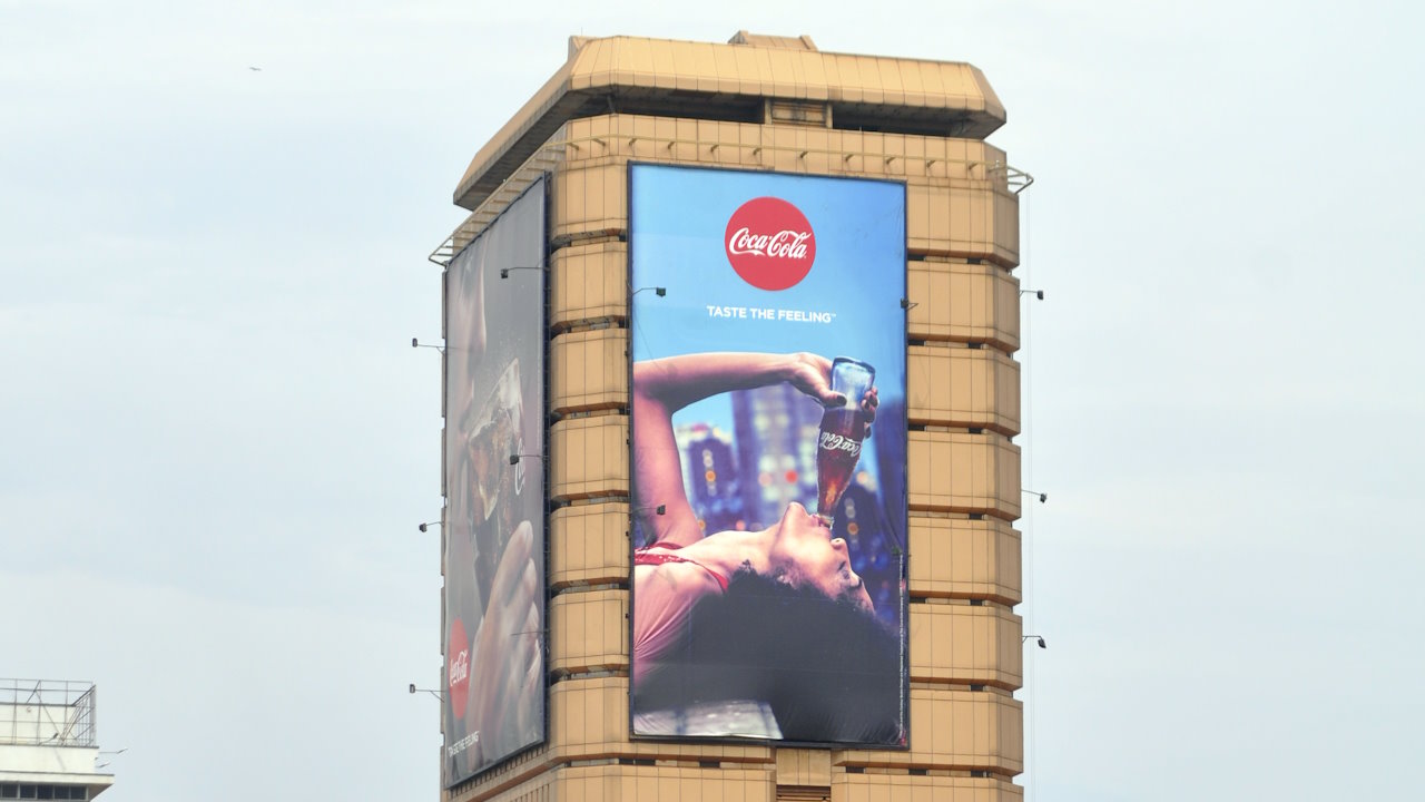 Billboard in Kampala advertising Coca-Cola. While Africa is largely absent from books on Coca-Cola, the company’s imprint on the continent is enormous. It is present in every nation. The story of Coke's arrival in Africa in the early 1900s is deeply, and often surprisingly, intertwined with key moments in African history. These include the end of Apartheid in South Africa and the emergence of postcolonial African nations. Coca-Cola is also what it is in Africa today because it became local, bending to the will of Africans in everything from sports to music to healthcare.