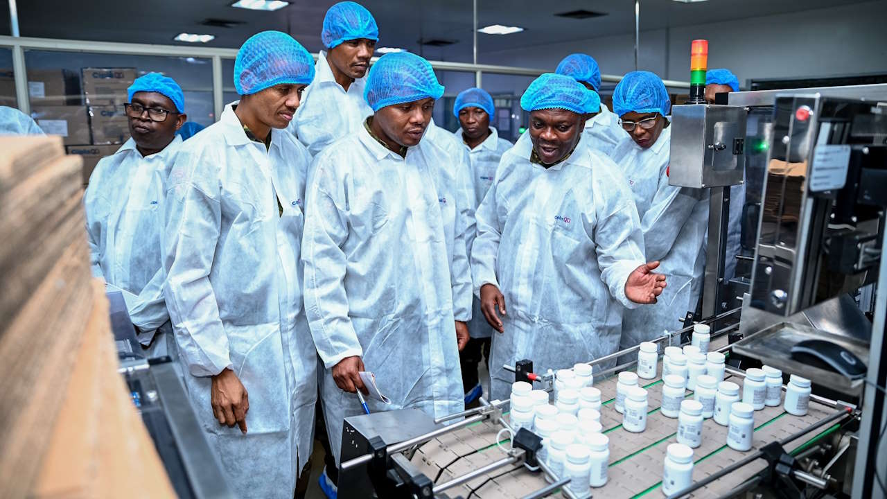 A group of men on a guided tour, directed by another man, in a pharmaceuticals factory