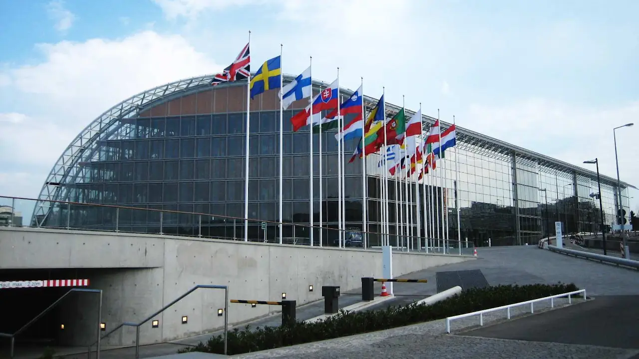 Glass-fronted European Investment Bank headquarters in Luxembourg, with flags of EU member states outside.