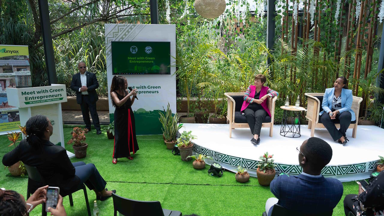 An outdoor discussion, with two female panellists seated in the chair, and other female holding a microphone and standing, as well as an audience