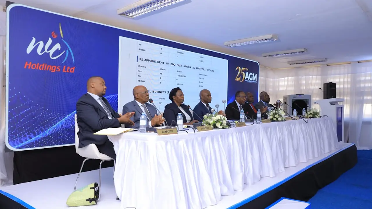 Seven people in dark suits seated at a long table draped in white cloth, with "Director" name plates, in front of a screen showing NIC Holdings' 25th AGM branding and a slide of the shareholder vote to reappoint BDO East Africa as auditors.