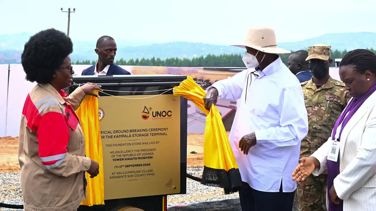 A group including President Museveni pulls back a yellow ribbon to reveal the Kampala Storage Terminal foundation plaque, with a soldier and officials looking on.
